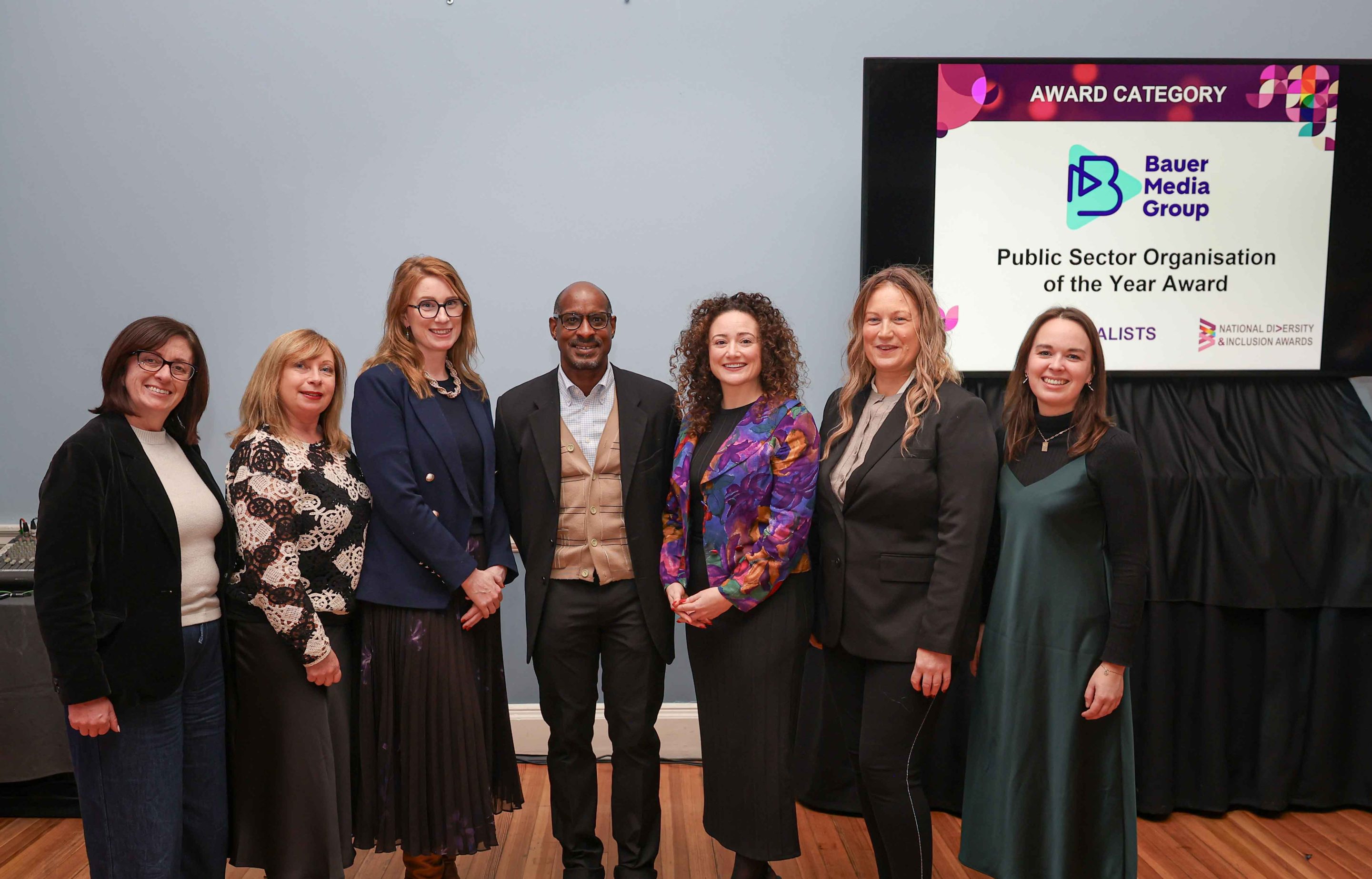 7 smiling people standing shoulder to shoulder