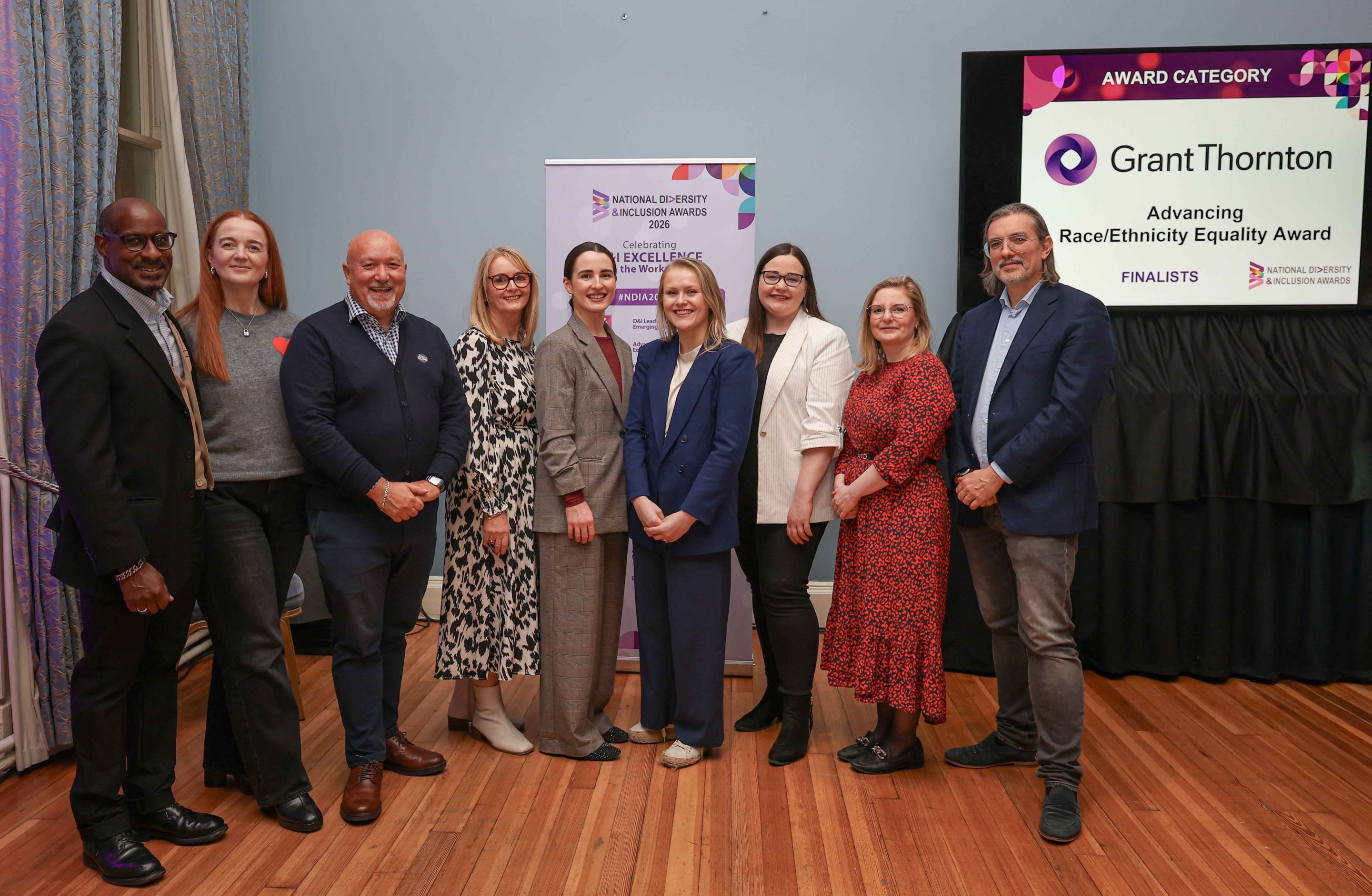 9 smiling people standing shoulder to shoulder