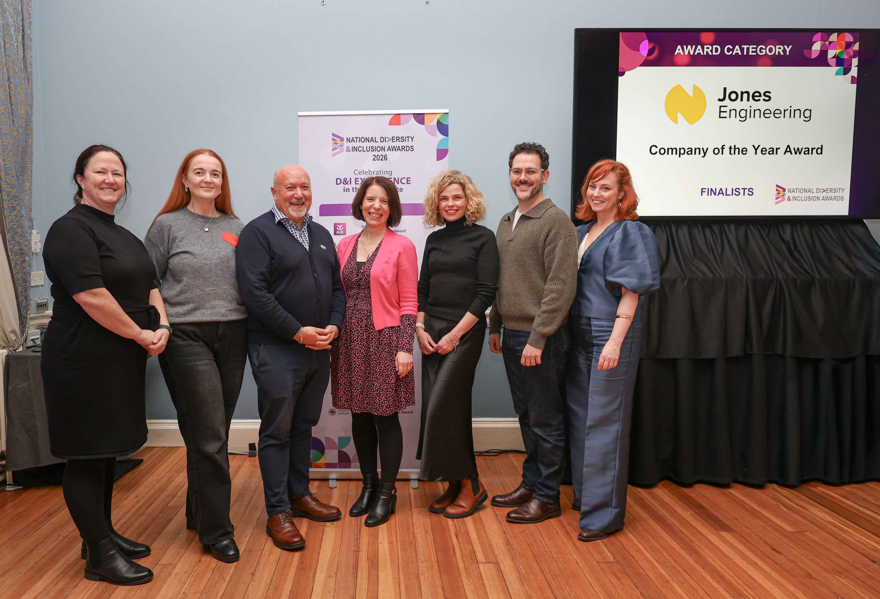 9 smiling people standing shoulder to shoulder