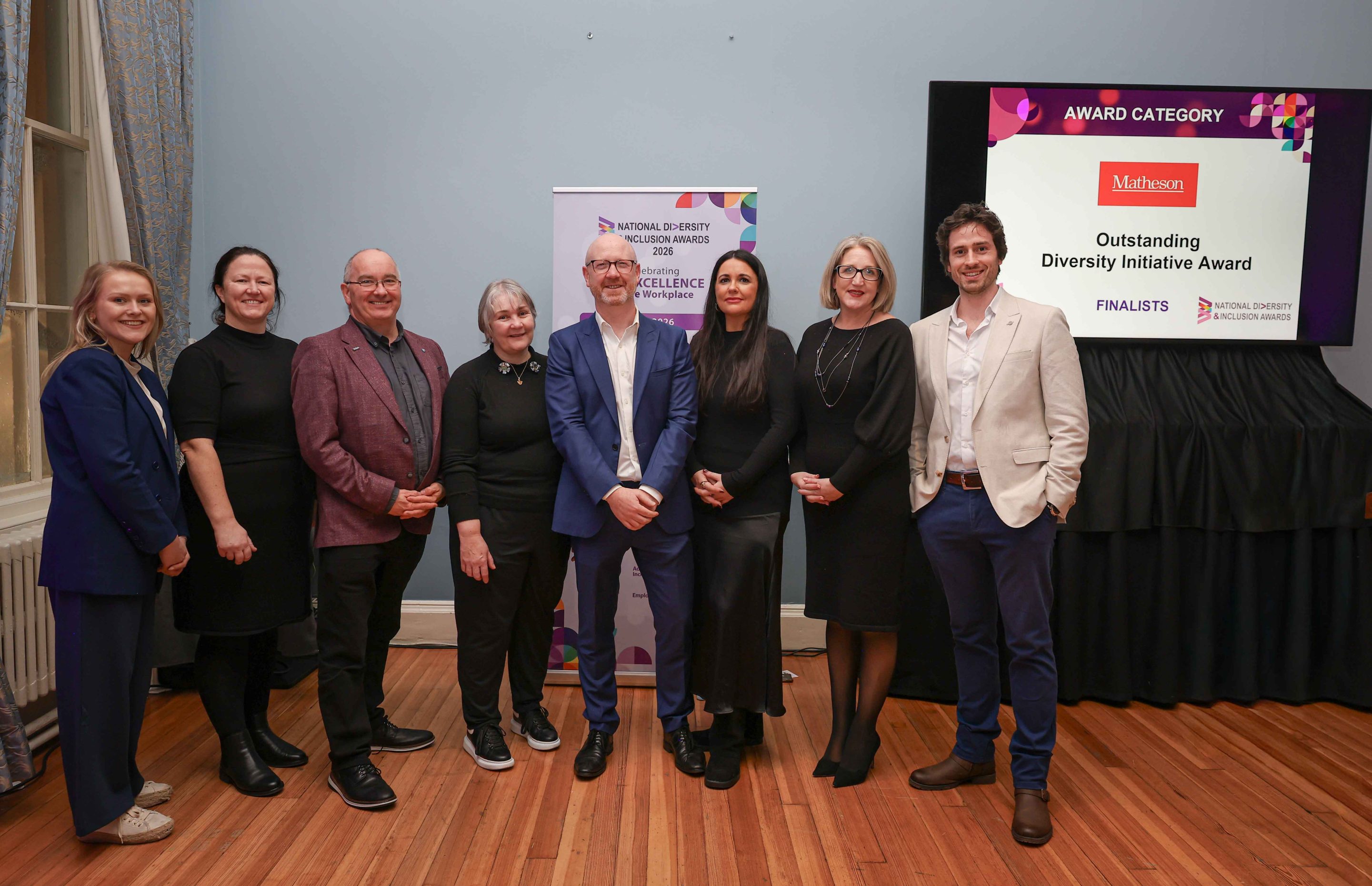 8 smiling people standing shoulder to shoulder