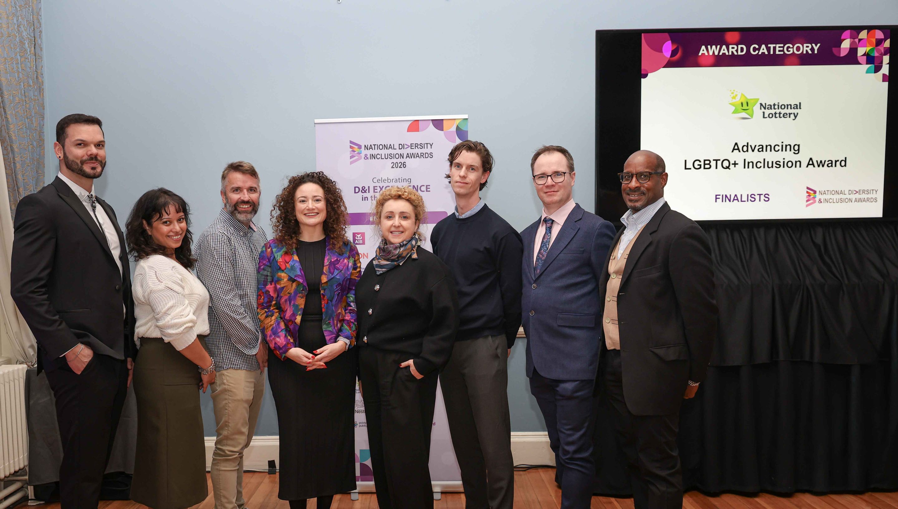 8 smiling people standing shoulder to shoulder