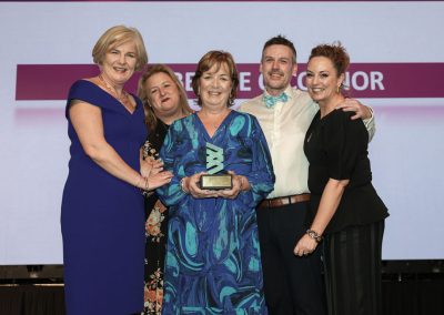 five smiling people standing shoulder to shoulder to the stage at an awards ceremony